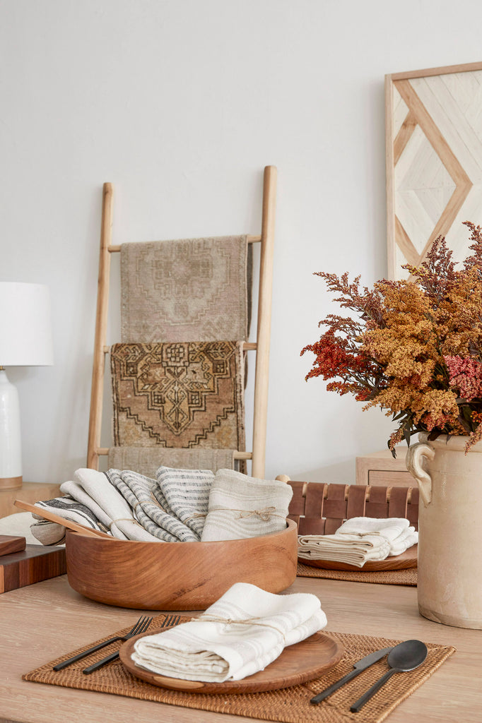 Styled picture of various Linen Hand Towels in a Teak Salad Bowl on an Oak Dining Table with Teak Plates, a Tenganan Placemat, an Italian Confit Pot and Woven Leather Strap Dining Chairs - Saddle. - Saffron and Poe