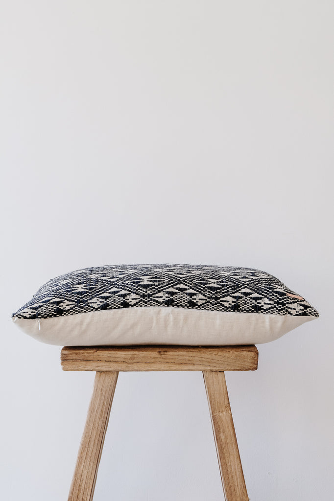 Side view of No. 19 - Antique Miao Lumbar Pillow on an Antique Stool against a white wall. - Saffron and Poe