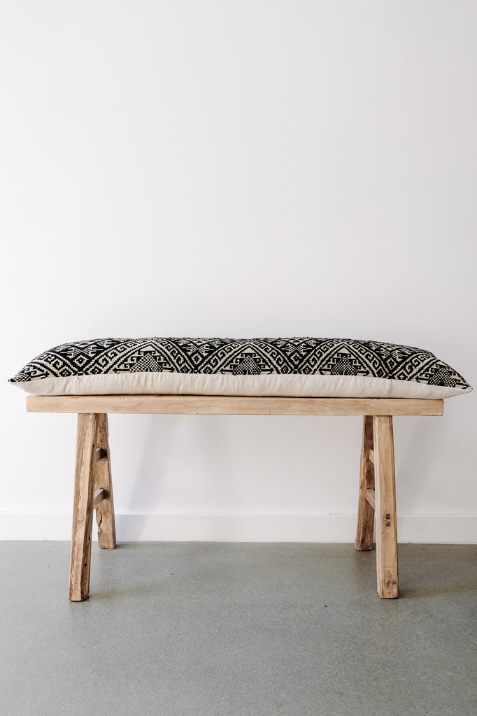 Side view of No. 22 - Antique Miao Lumbar Pillow (Ex-Large) on an Antique Chinese Bench against a white wall. - Saffron and Poe