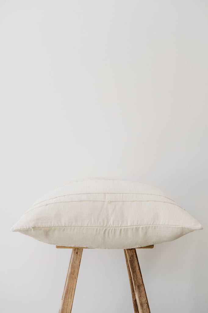 Side view of No. 50 Azulina Ivory with Ivory Stripe Handwoven Columbian Pillow on an Antique Stool against a white wall. - Saffron + Poe