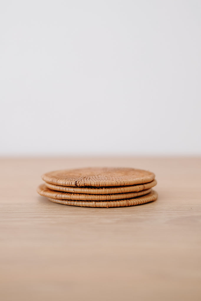 Front view of Tenganan Coaster - Set of 4 on an oak dining table against a white wall. - Saffron and Poe
