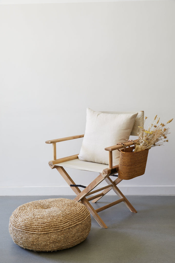 Styled view of the Ivory Director's Chair Pillow on the Oatmeal Director's Chair with the Tenganan Side Basket and Natural Woven Pouf against a white background and concrete flooring. - Saffron and Poe