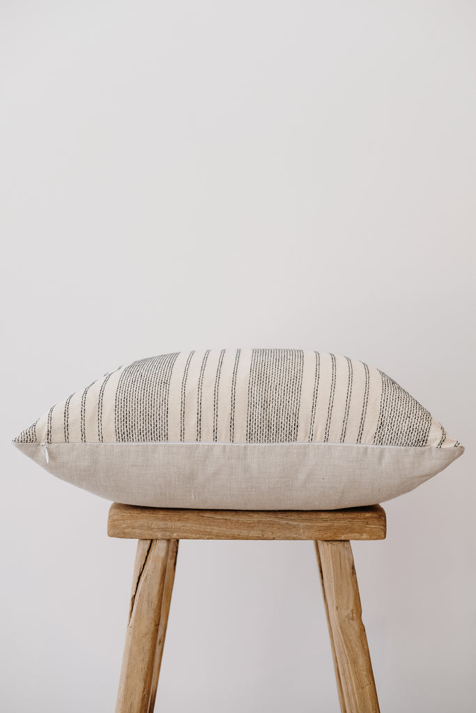 Side view of No. 03 - Hmong Hemp Batik Pillow on an Antique Stool against a white wall. - Saffron and Poe