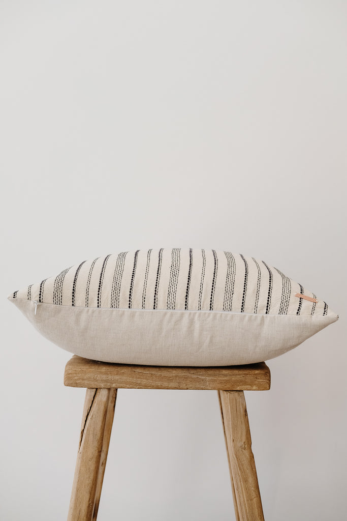 Side view of No. 04 - Hmong Hemp Batik Pillow on an Antique Stool against a white wall. - Saffron and Poe