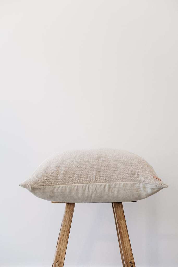 Side view of No. 17-Hmong Hemp Batik Pillow on an Antique Stool against a white wall. - Saffron and Poe