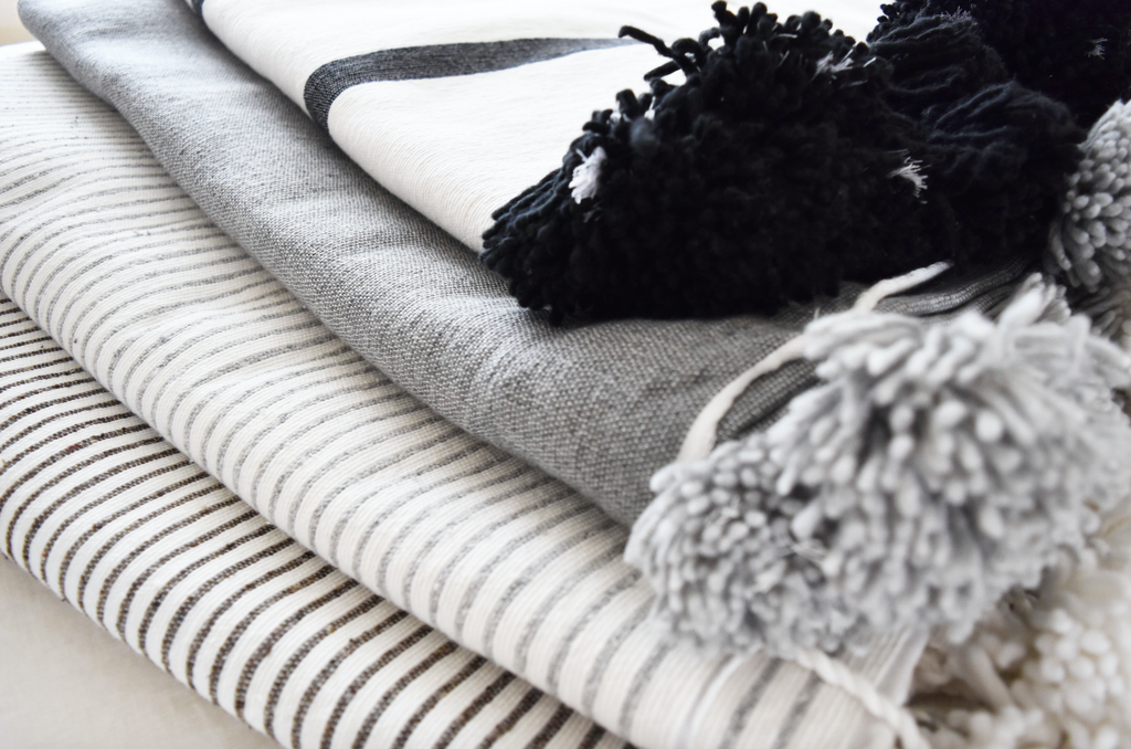 Three Bohemian blankets stacked and styled with Moroccan Pom Bed Throw - Dark Grey and White Stripes. Hand-woven in Marrakech using wooden looms. - Saffron and Poe