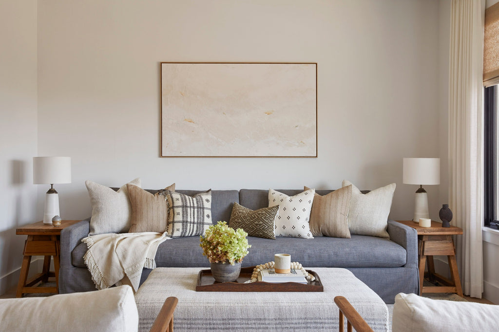 Styled view of our Handwoven Colombian Throw in ivory draped over a sofa in a living room setting which includes our Ceramic Lamps, Vintage End Tables, Bhujodi pillows, and Kaleen Cameron art work. - Saffron and Poe.