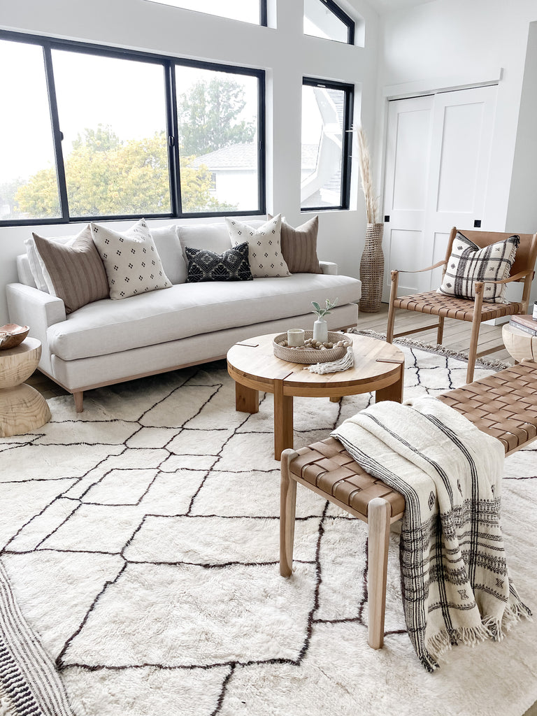 Styled Brown Checkered Pillow with Beige Embroidered Pillow and an Antique Miao Pillow with Bhujodi textiles and a Woven Leather Strap Bench and a Safari Chair. - Saffron and Poe