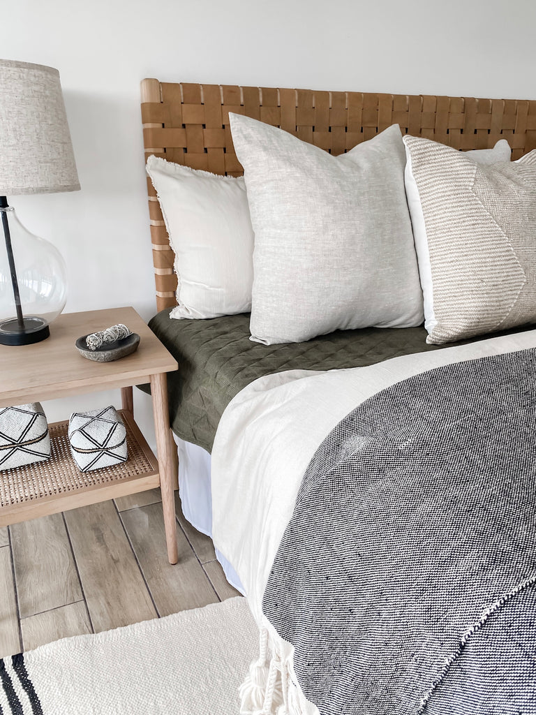 Close up styled Natural Linen Pillow with a Woven Leather Strap Headboard on a Turkish Kilim Rug with Bali Baskets. - Saffron and Poe