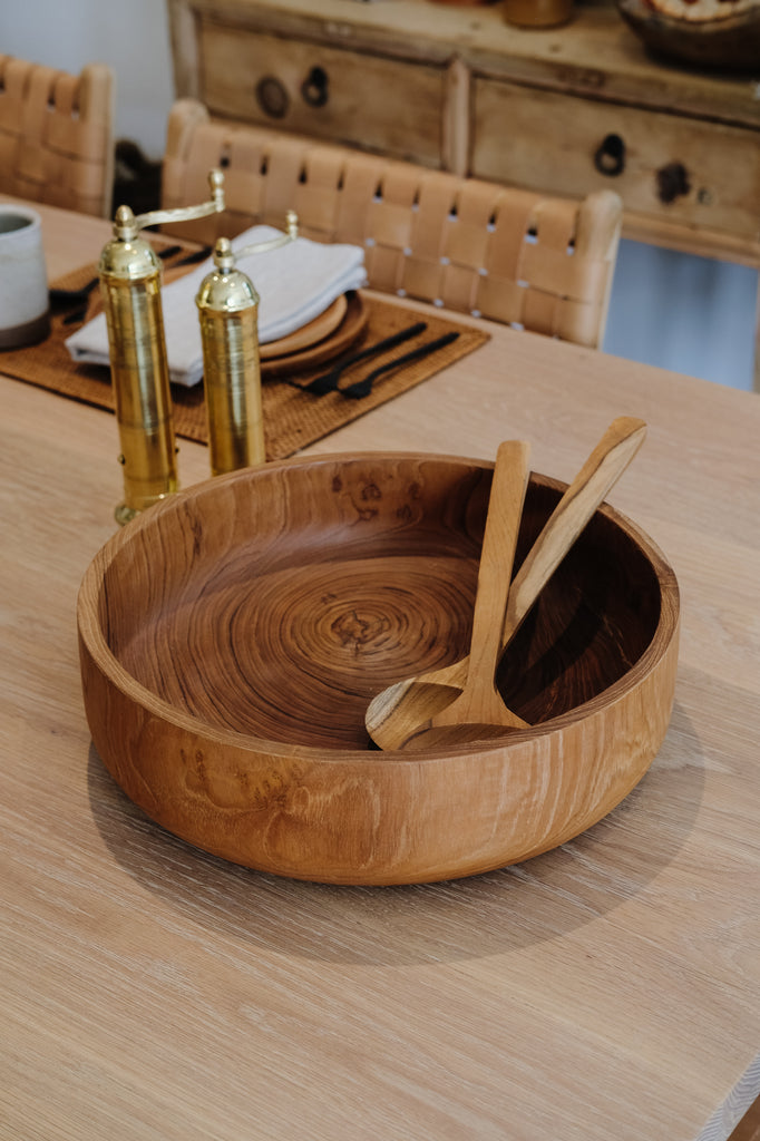 Styled Teak Salad Bowl with a Pair of Wooden Tongs, some Brass Grinders, Tenganan Placemats, and Teak Plates on an Organic Edge Oak Dining Table. - Saffron and Poe