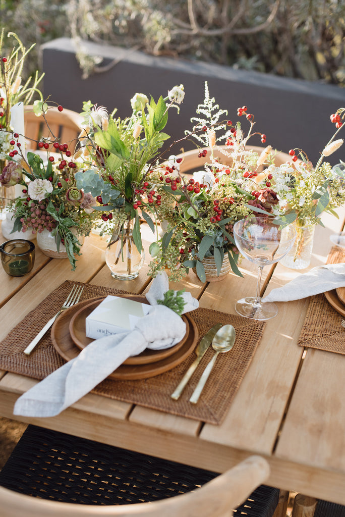 Woven Tenganan Placemat with Teak Plates and Natural Woven Napkin on an outdoor table setting with holiday florals. - Saffron and Poe