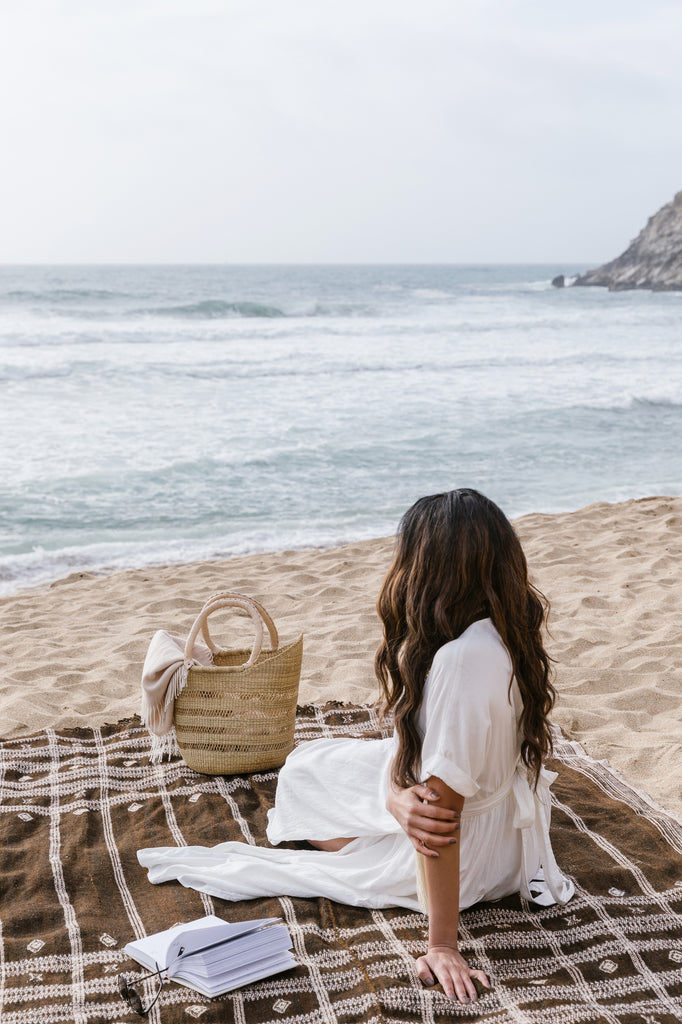 Styled view of Woven Sisal Farmer's Market Tote with a Handwoven Bhujodi Blanket - Dark Brown with a beach background. - Saffron and Poe