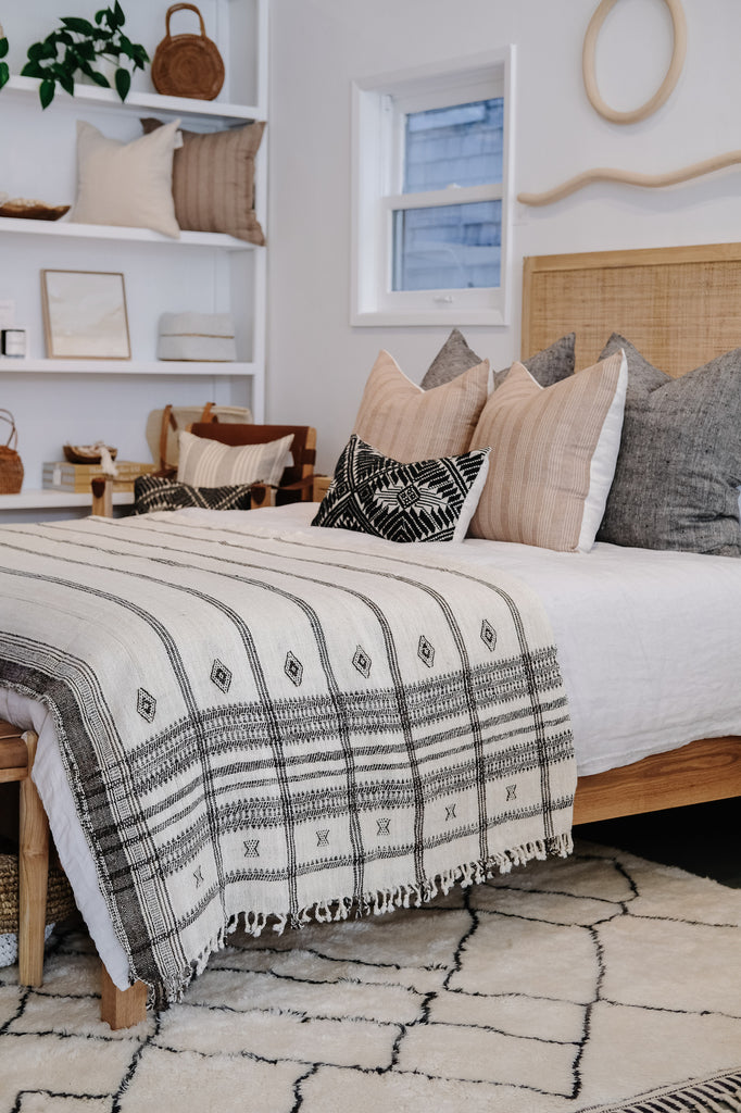 Styled angled view of Handwoven Bhujodi Bed Throw - Natural - with Rattan Headboard and Linen Pillows - Saffron + Poe