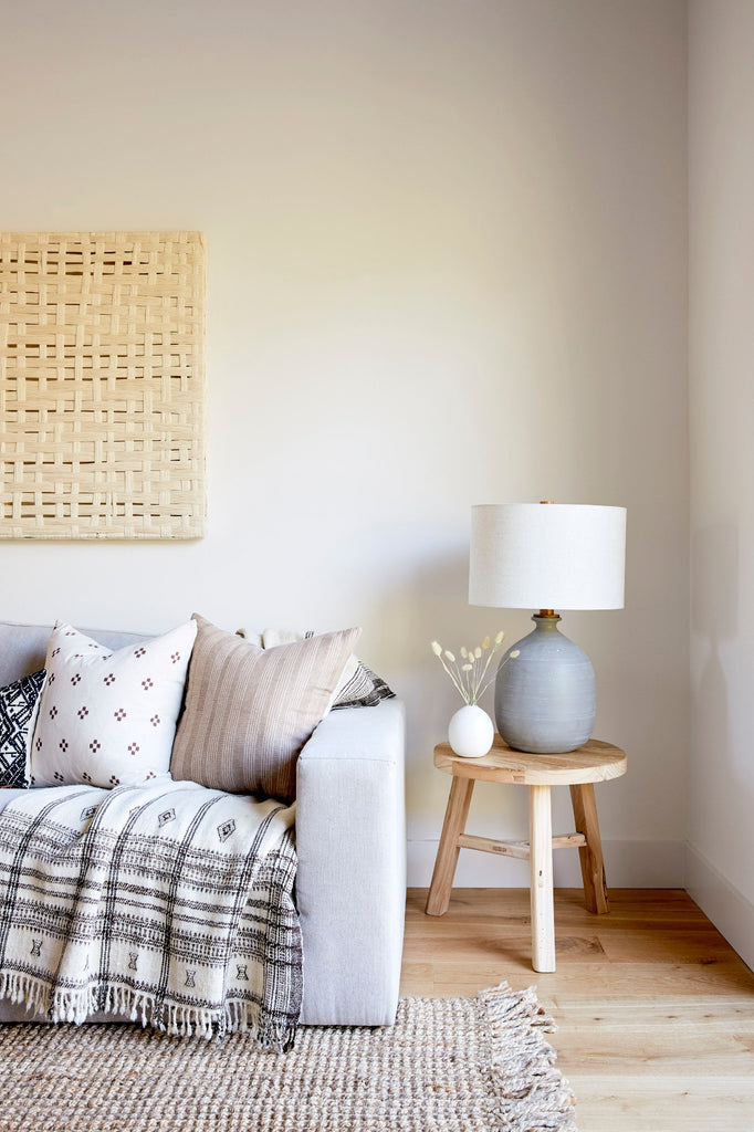 Handwoven Bhujodi Blanket in Natural on a light blue sofa with Brown Checkered Pillow, Beige Embroidered Pillow, and Vintage Round Side Table. - Saffron + Poe