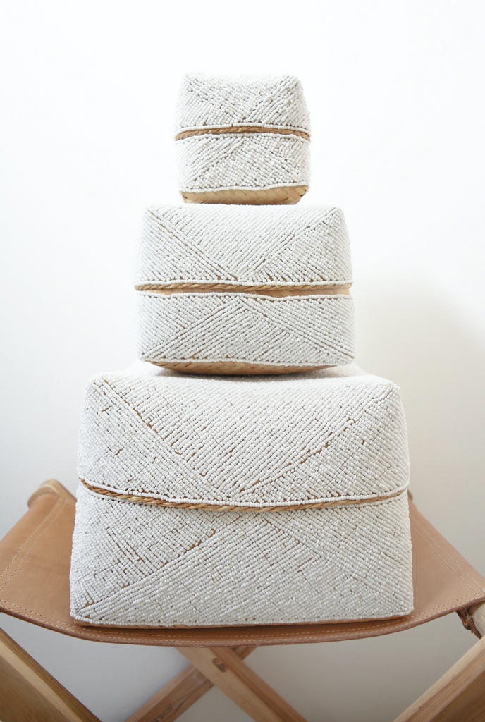 Three Hand-Beaded Bali Storage Baskets in Solid White stacked on each other sitting on a leather strapped stool. Handmade in Bali using woven bamboo- Saffron and Poe