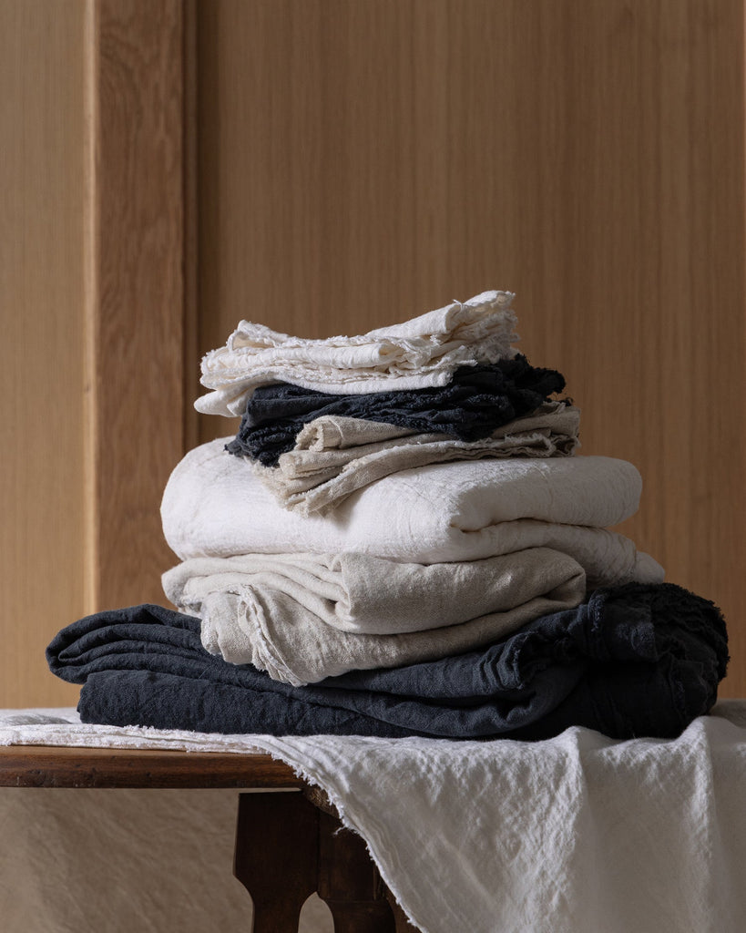 Stack of folded Philo Linen Napkins and placemats on a wooden table with a wooden wall background