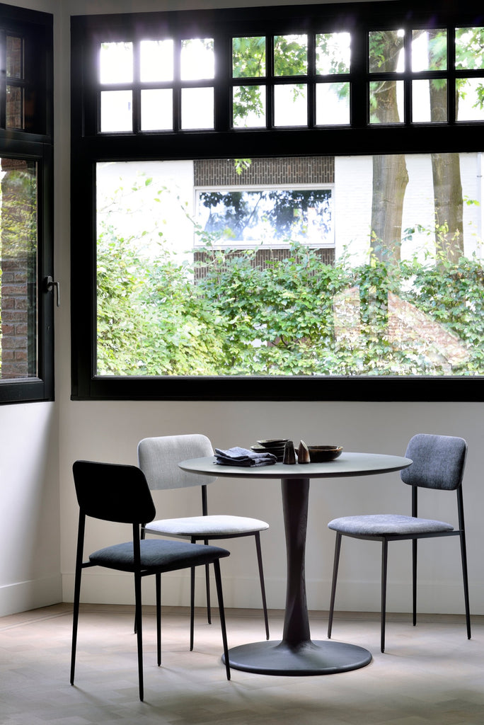 Black Oak Torsion Dining Table in bright dining room with large windows and concrete floor. - Saffron and Poe, Ethnicraft