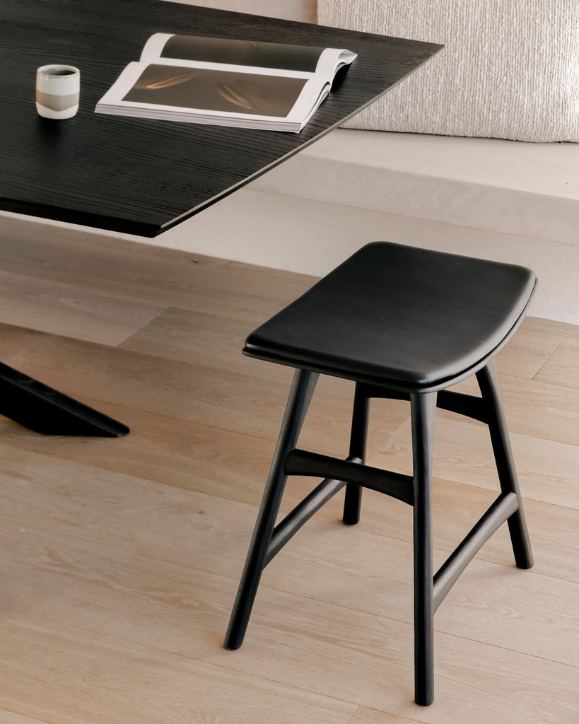 Black Oak Mikado Dining Table up close with stool and wood floors, with a magazine and cup styled on top. - Saffron and Poe, Ethnicraft