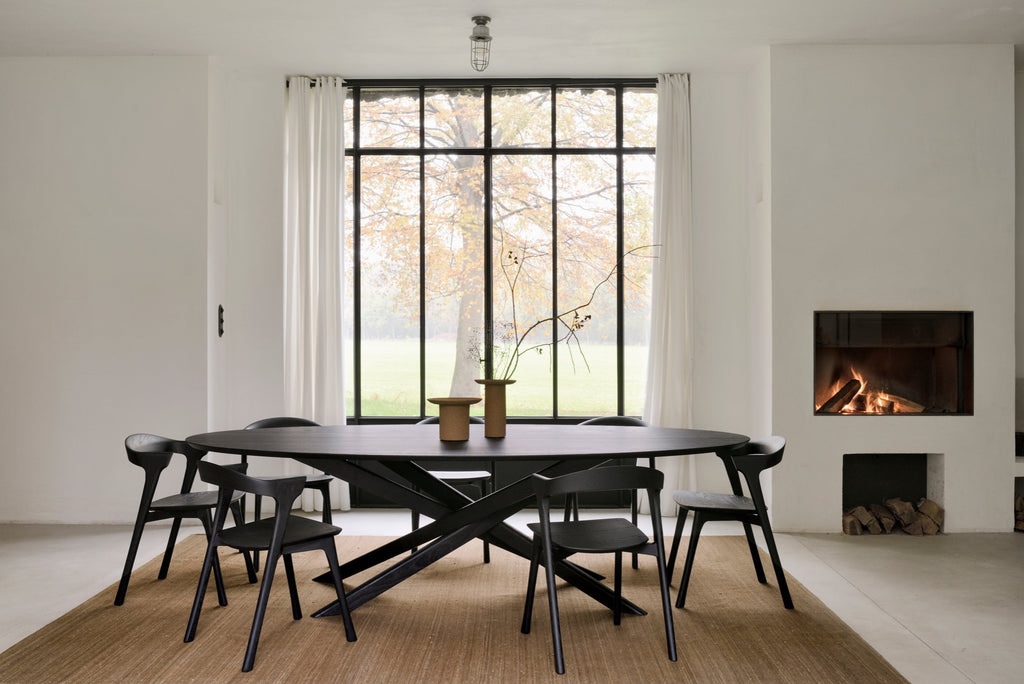 Black Oak Oval Mikado Dining Table and black oak bok dining chairs in bright dining room with white linen draperies and plaster fireplace, with ceramiv vases styled on top. - Saffron and Poe, Ethnicraft