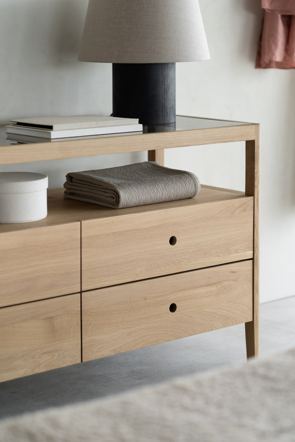 Spindle dresser in European white oak with four drawers, open shelf, and glass top, featuring sleek lines and rounded edges.