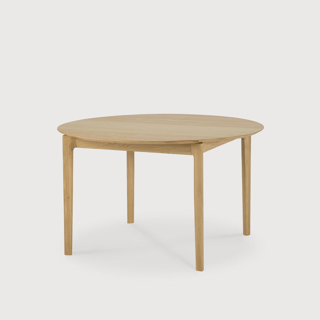 Oak Bok Round Extendable Dining Table with white background at an angle in closed position, with floating table top and beautiful wood joinery. - Saffron and Poe, Ethnicraft
