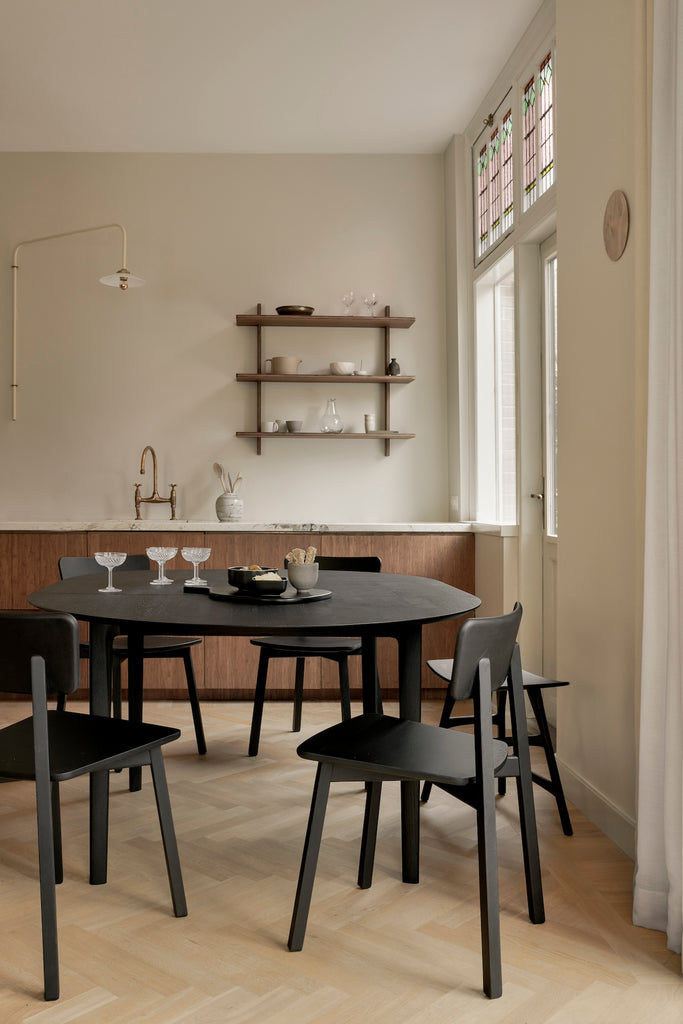 Black Oak Bok Round Extendable Dining Table and Black Oak Bok chairs in kitchen with herringbone wood flooring, featuring float top and beautiful wood joinery. - Saffron and Poe, Ethnicraft.