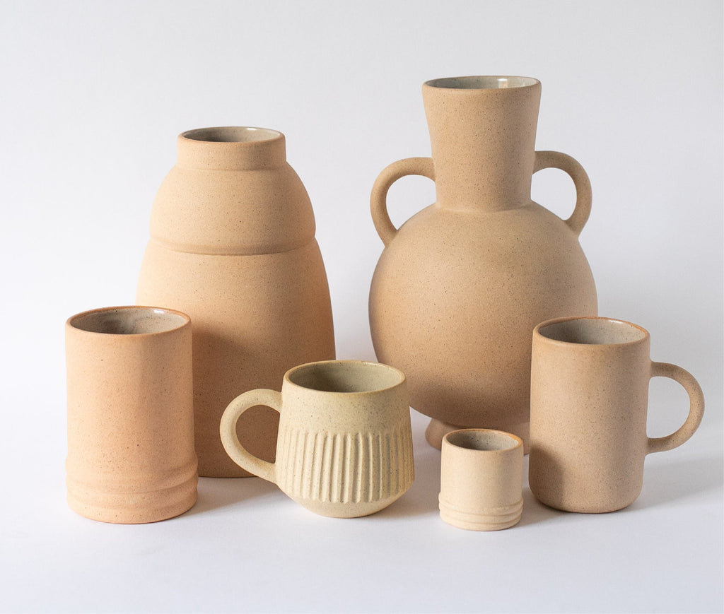Collection of light terracotta ceramic vases and mugs on a white background