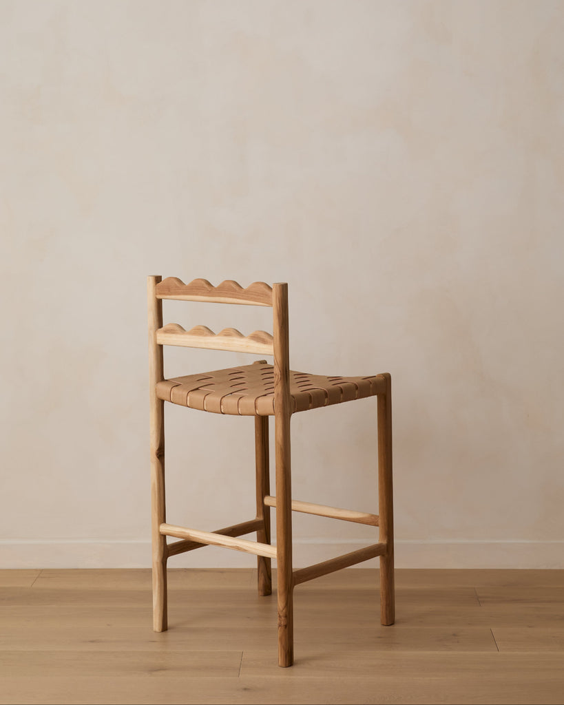 Aegean scalloped counter stool with woven seat on white oak flooring against a beige wall. Saffron and Poe