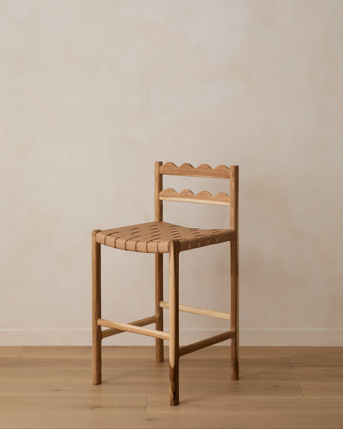Aegean scalloped counter stool with woven seat on white oak flooring against a beige wall. Saffron and Poe