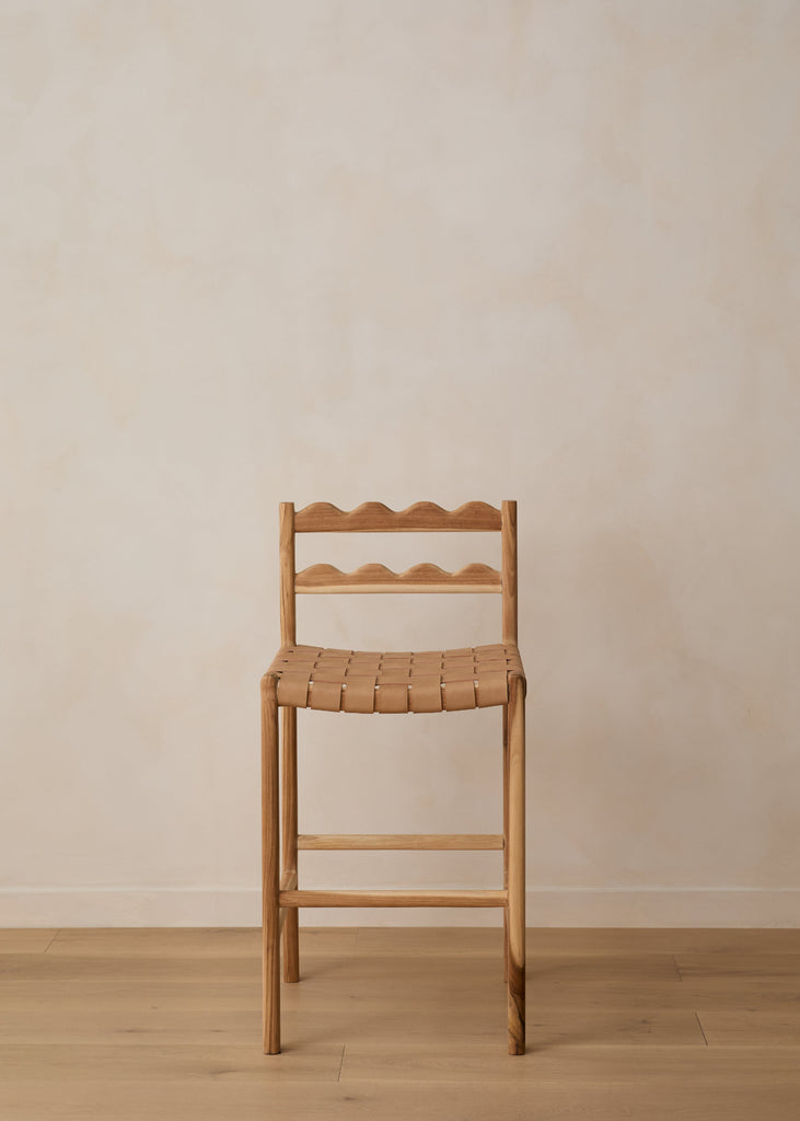 Aegean scalloped counter stool with woven seat on white oak flooring against a beige wall. Saffron and Poe