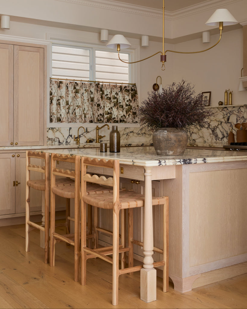 Aegean scalloped counter stool with woven seat in a white oak kitchen with marble counters. Saffron and Poe