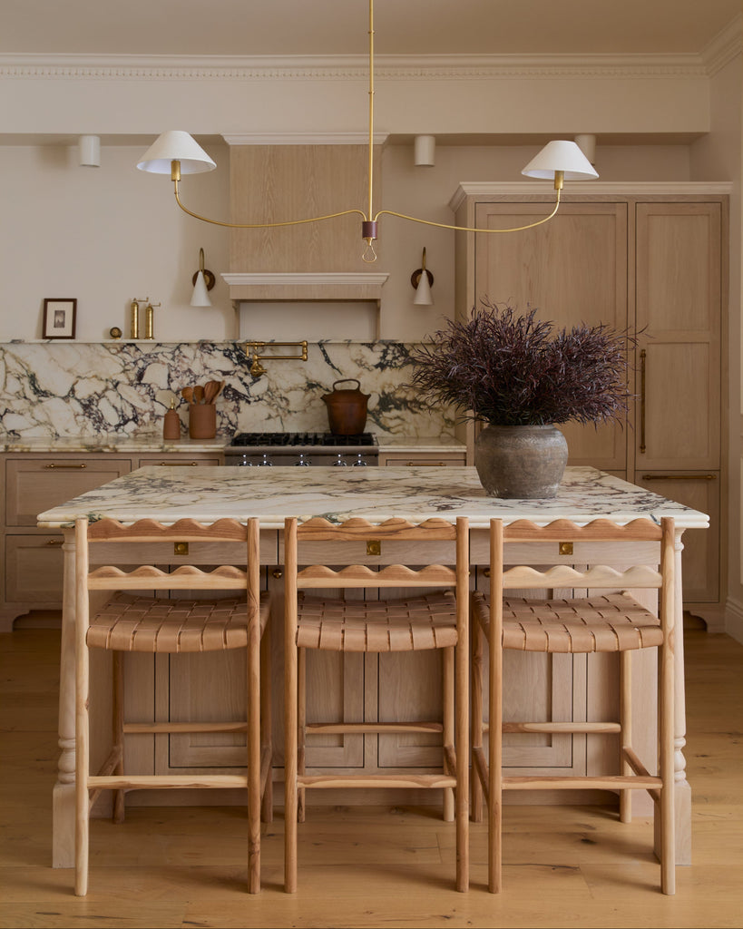 Aegean scalloped counter stool with woven seat in a white oak kitchen with marble counters. Saffron and Poe