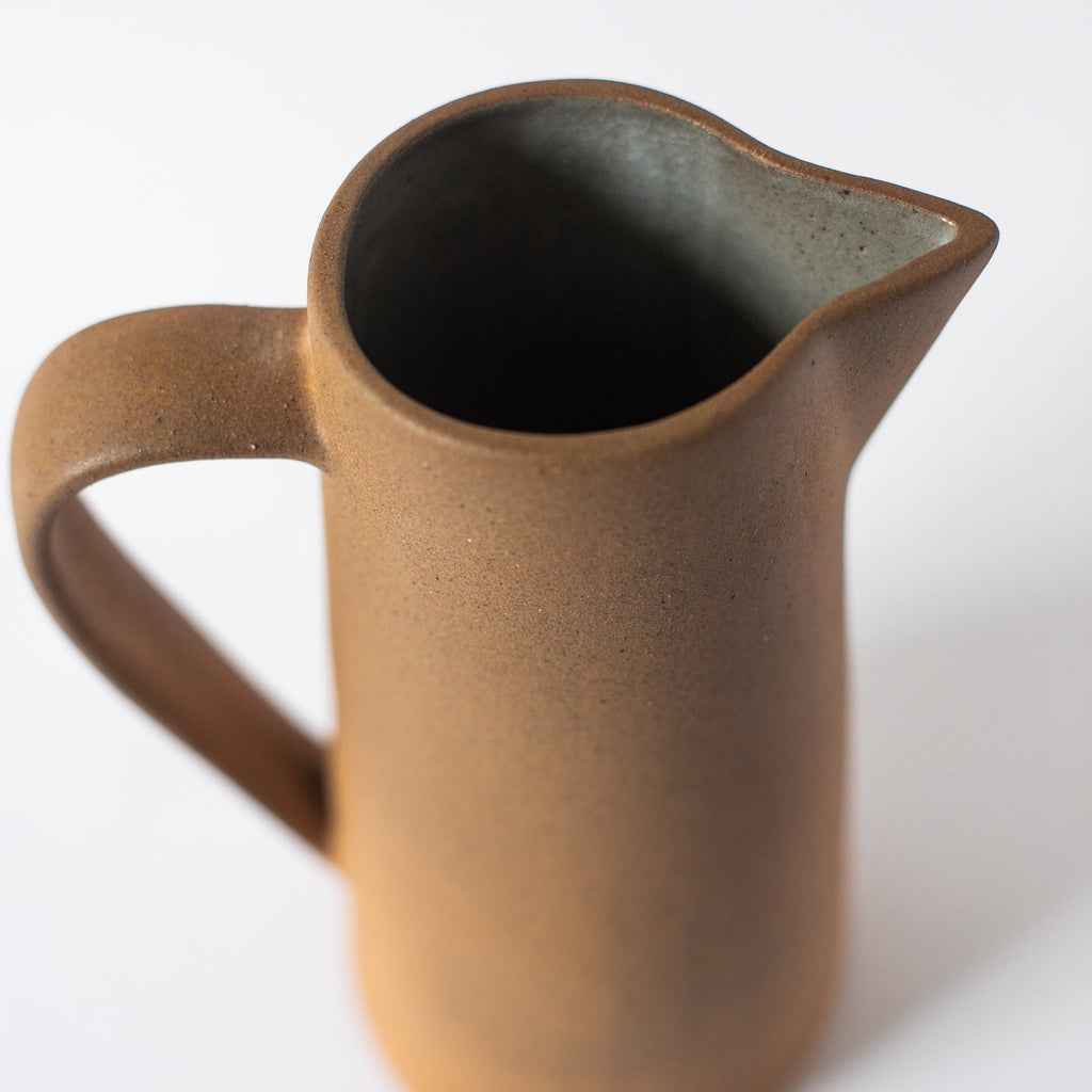 Handcrafted tall ceramic pitcher with earth tone clay textures and glazed interior
