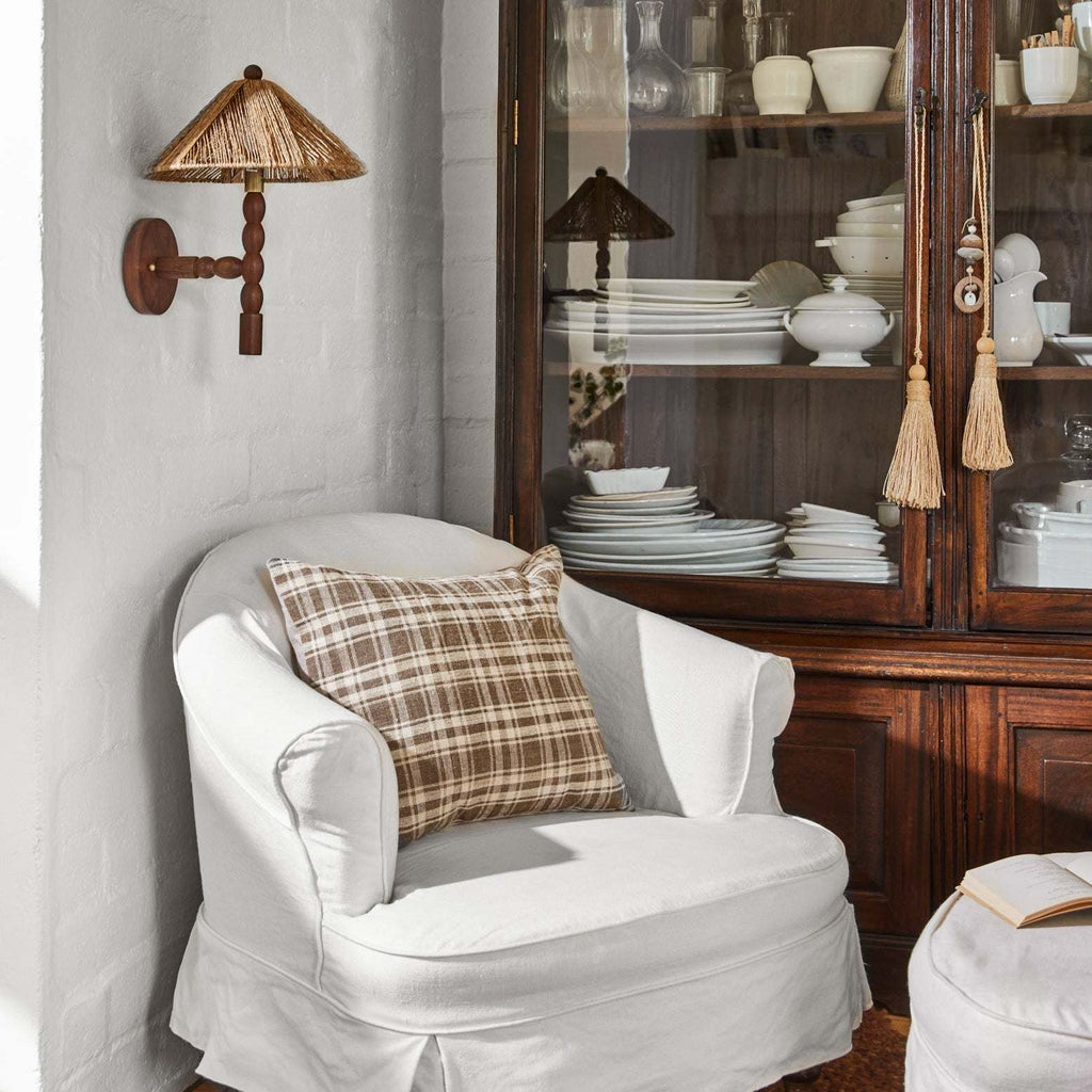 White armchair with a plaid pillow and Alhambra wall Sconce in front of a wooden china cabinet.