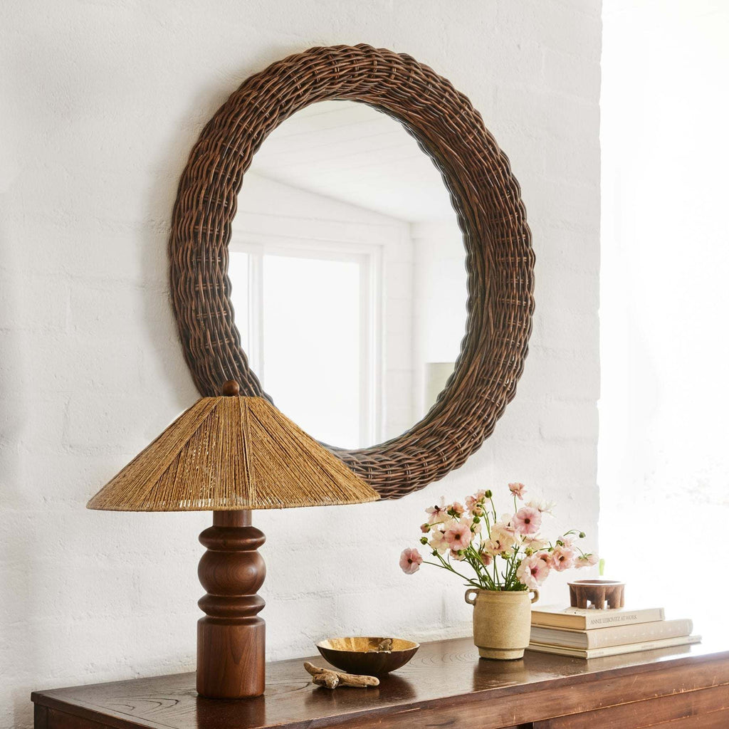 Round wicker mirror on a wall above a wooden console table with an Alhambra Table Lamp