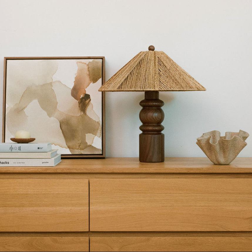 Wooden dresser with an Alhambra table lamp, books, and artwork on top against a white wall.