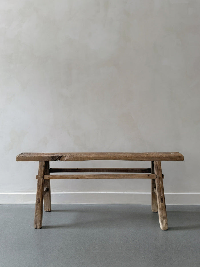 Vintage wood bench agains a limewash wall and concrete floor 