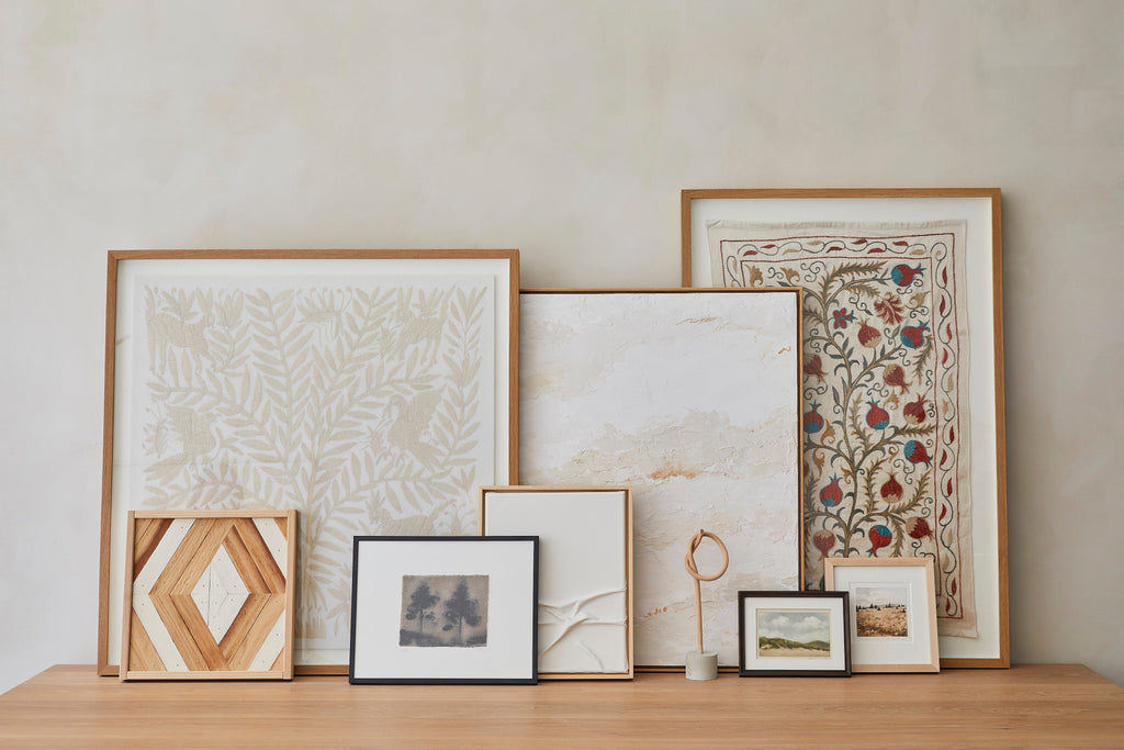 Saffron + Poe Art collection in front of beige limewashed wall on oak table.
