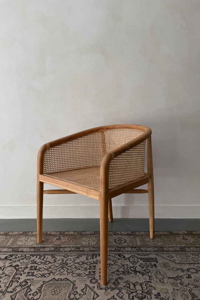Wooden accent chair with wicker backrest on a textured rug against a plain wall
