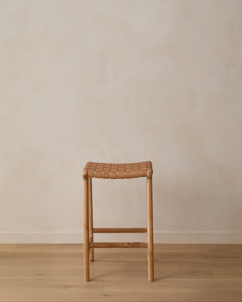 Beige Woven Leather Counter Stool on oak wood floor in front of limewashed wall. Saffron + Poe