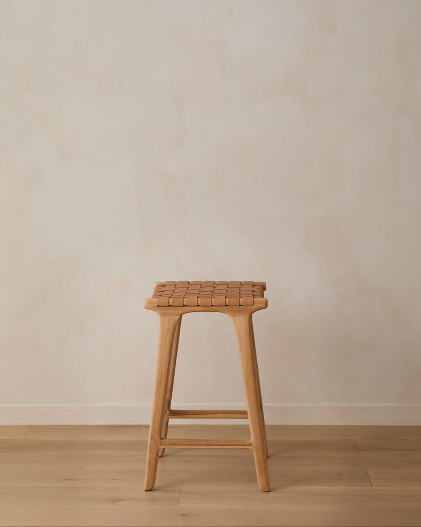 Beige Woven Leather Counter Stool on oak wood floor in front of limewashed wall. Saffron + Poe