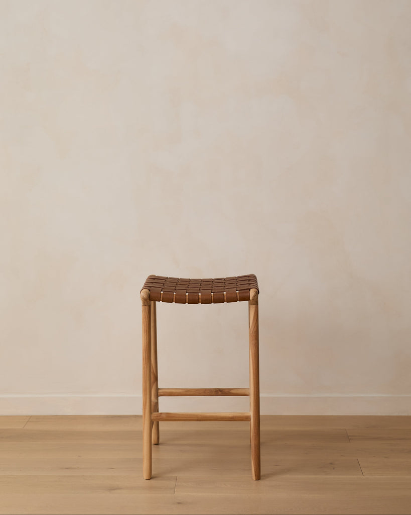 Backless woven leather counter stool on oak floor against limewashed wall. Saffron + Poe