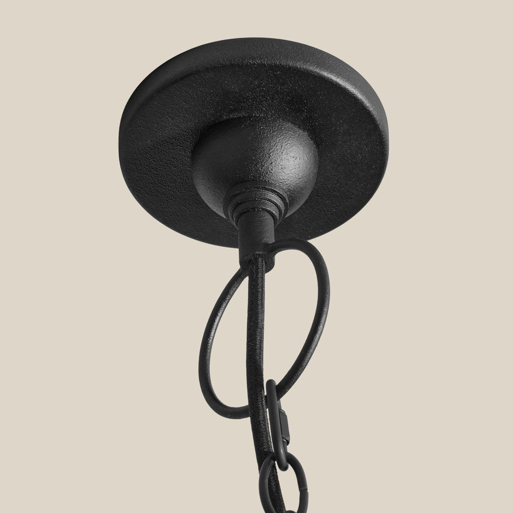 A close-up of a black metal ceiling light fixture canopy and hanging chain against a solid beige background.