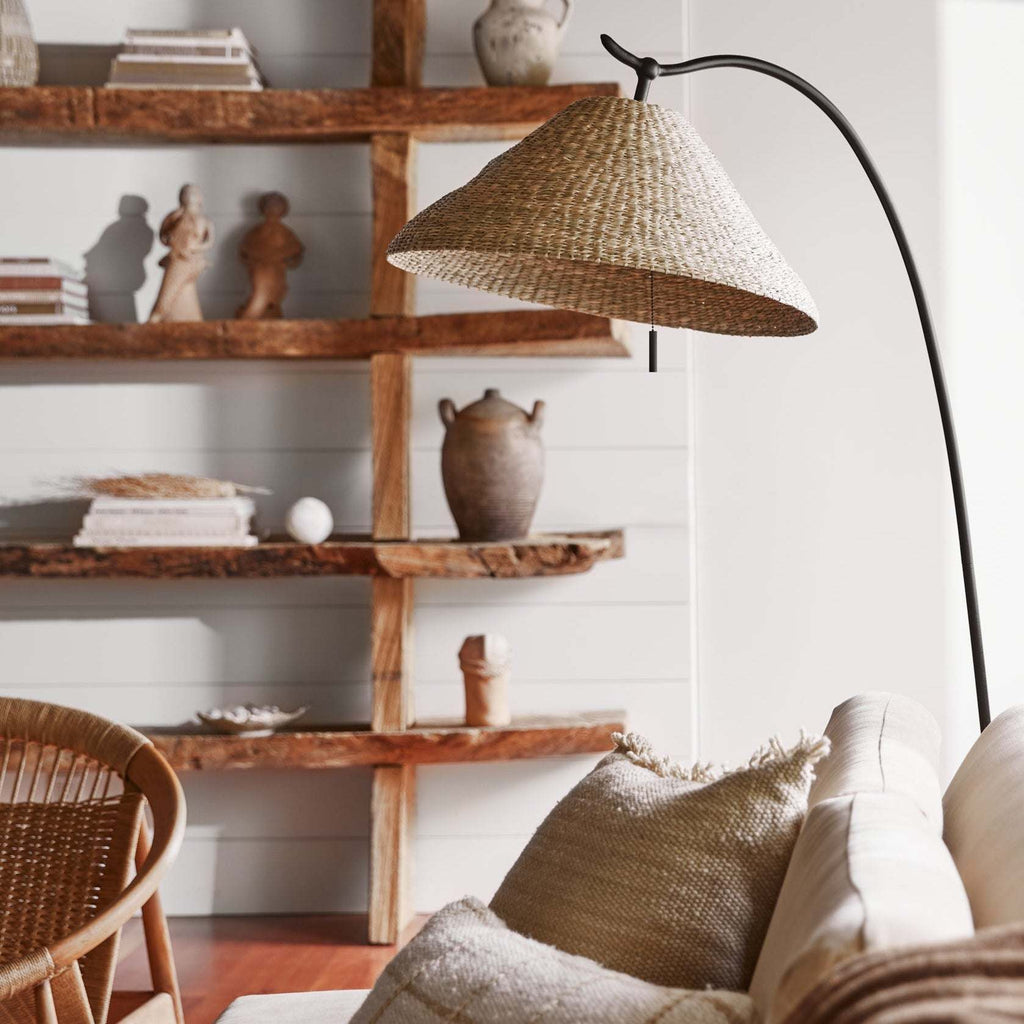 Living room with wooden shelves, wicker chair, and a Bainbridge floor lamp with woven shade.