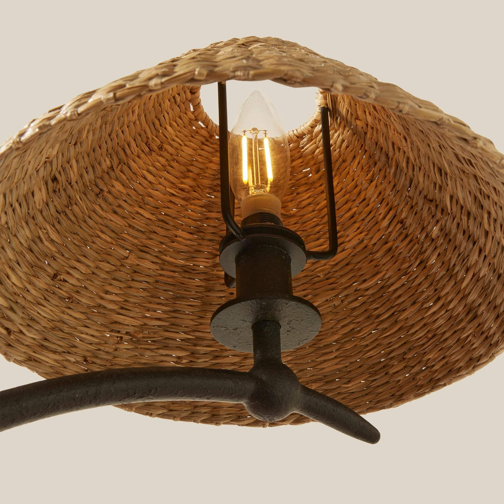 Wicker lampshade from Bainbridge large chandelier with a lit bulb on a neutral background