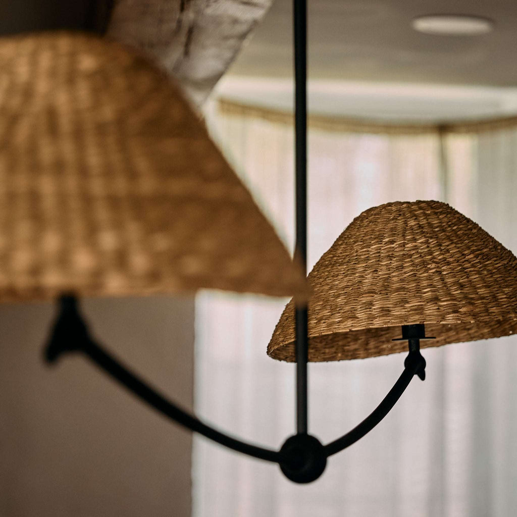 Two woven lampshades of a Bainbridge Linear Pendant hanging from a black cord against a blurred indoor background.