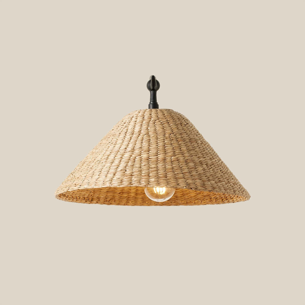 Bainbridge Oversized Swing Arm Sconce with a woven seagrass shade and an exposed bulb on a beige background.