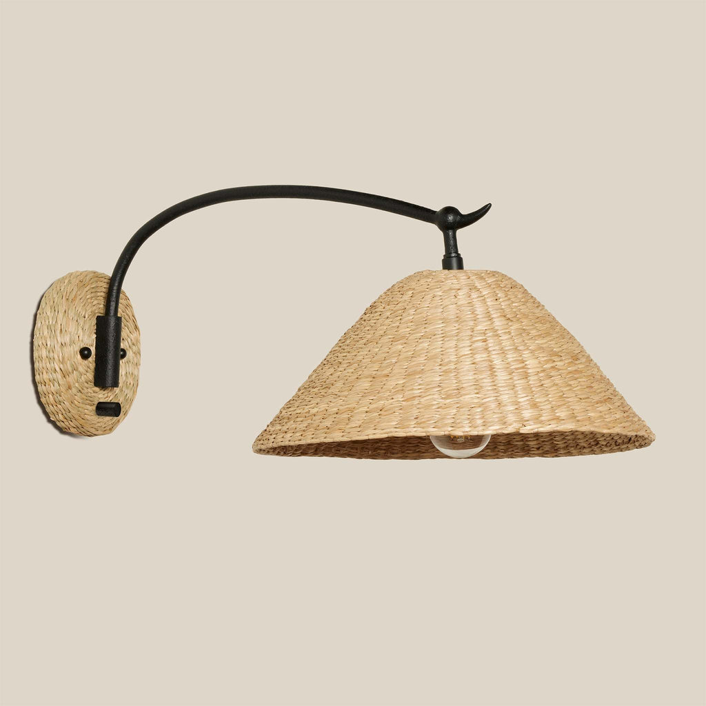 Wall-mounted Bainbridge Sconce with woven seagrass shade and black metal arm on a beige background.