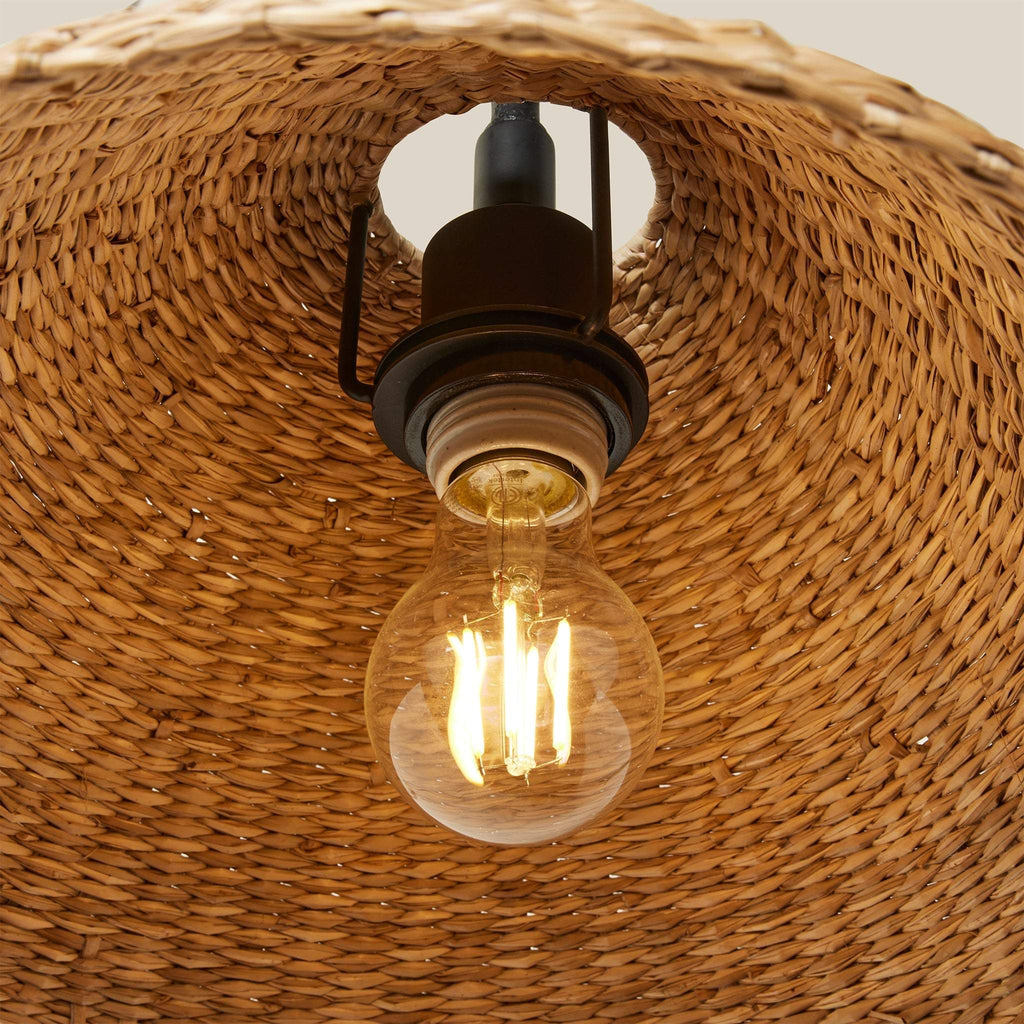 Edison light bulb inside woven seagrass shade for Bainbridge Oversized Swing Arm Sconce.
