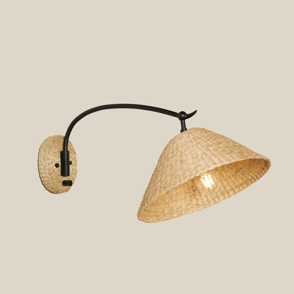 Wall-mounted Bainbridge sconce with woven seagrass shade and black metal arm on a beige background.
